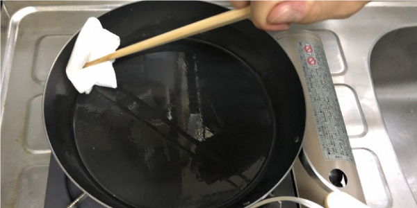 菜箸で持ったペーパーで鉄フライパンに油を広げる作業