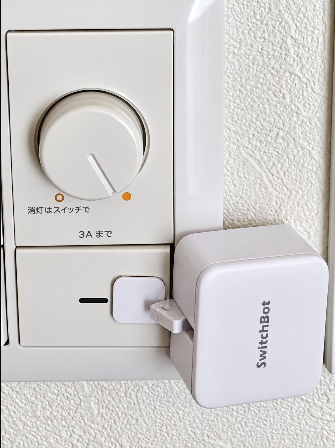 筆者の壁スイッチに後付けしたSwitchBotボットと、スイッチを押すアーム